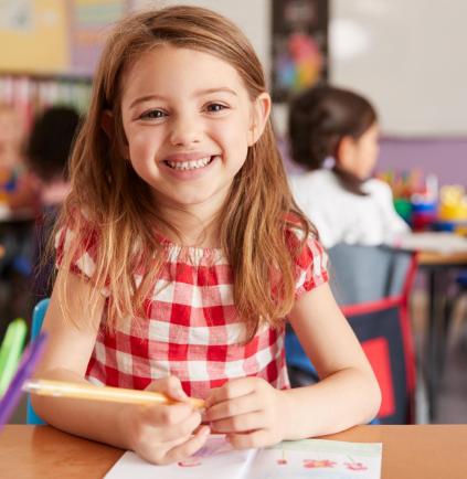 Portrait Of Smiling Female Elementary School Pupil Working At Desk